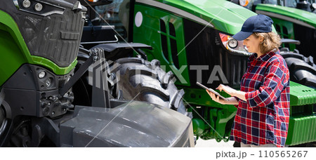 Woman farmer with a digital tablet on the background of an agricultural tractor. 110565267