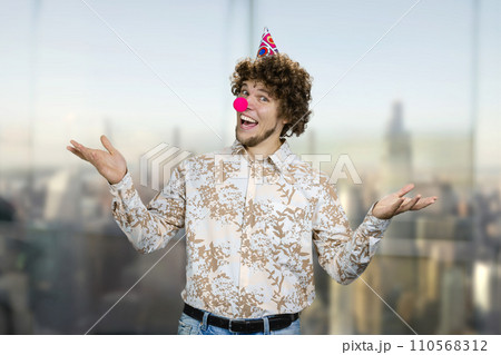 Portrait of a young caucasian guy with curly hair wearing a clowns nose. Happy birthday concept. Portrait of a young caucasian guy with curly hair wearing a clowns nose. Happy birthday concept. 110568312