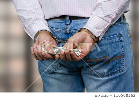 Close up male hands in handcuffs holding money. Crime and bribery concept. 110568362