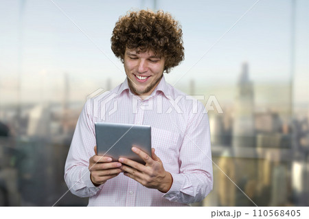 Excited young happy caucasian man holding a tablet pc device. Guy playing mobile videogame app or watching digital video stream holding cell phone indoors. 110568405