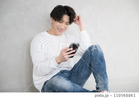 壁に寄りかかりスマホを持つ男性 110568861