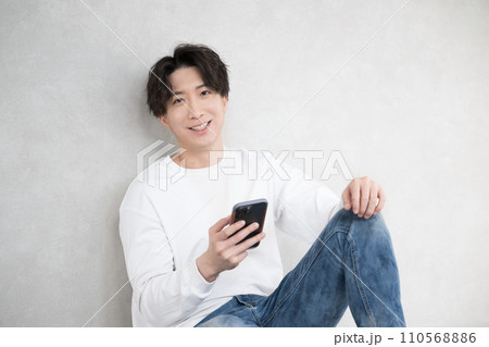 壁に寄りかかりスマホを持ちカメラ目線のハンサム男性の上半身 壁に寄りかかりスマホを持ちカメラ目線のハンサム男性の上半身 110568886