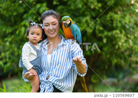 happy mother and daughter feeding blue-and-yellow macaw (Ara ararauna) bird on hand happy mother and daughter feeding blue-and-yellow macaw (Ara ararauna) bird on hand 110569607