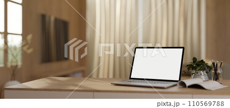 Modern home workspace with a white-screen laptop and stationery on a table in a modern living room. Modern home workspace with a white-screen laptop and stationery on a table in a modern living room. 110569788