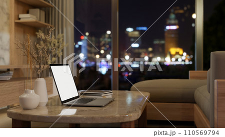 A laptop mockup on a luxury marble coffee table in a modern apartment living room at night. 110569794