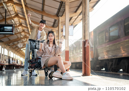 Cheerful couple are walking down the platform with a cart, commuting by a train at a railway station Cheerful couple are walking down the platform with a cart, commuting by a train at a railway station 110570102