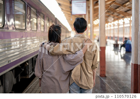Back view image of a lovely Asian couple wrapping around shoulder while walking down the platform. 110570126