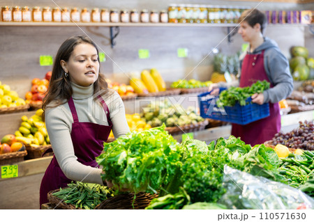 Female seller in uniform working in grocery shop, posing with salad and spinach 110571630
