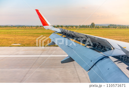 View of airplane wing, blue skies and green land during landing. Airplane window view. 110571671