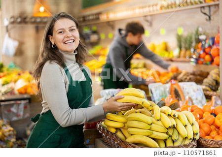 Young woman seller laying out bananas on counter Young woman seller laying out bananas on counter 110571861