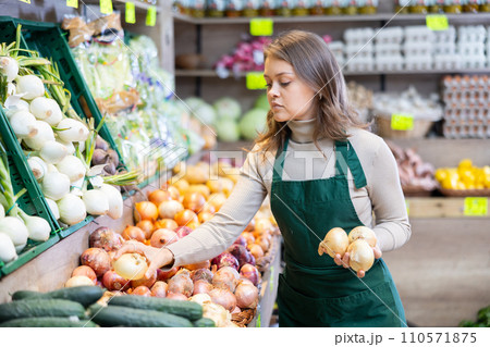 Female seller working in supermarket and lays out onions on counter 110571875