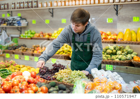 Smiling male seller in apron displaying assortment of grape at supermarket Smiling male seller in apron displaying assortment of grape at supermarket 110571947