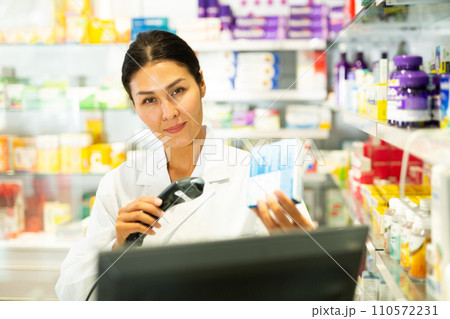 Portrait of female pharmacist working at the cash register in pharmacy - scans barcode on medicine package Portrait of female pharmacist working at the cash register in pharmacy - scans barcode on medicine package 110572231