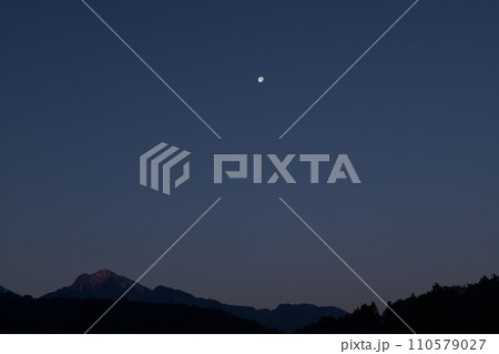 頂を赤く染める南アルプス甲斐駒ケ岳と西に傾いた月齢16.1の月 110579027