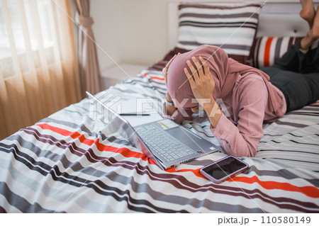 woman in veil dizzy while using laptop while lying on bed 110580149