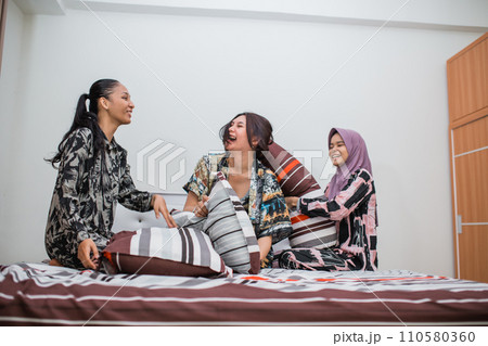 three girls in pajamas laugh while joking together in bed three girls in pajamas laugh while joking together in bed 110580360