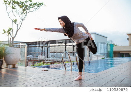 young woman in hijab doing dancers pose by the resort swimming pool 110580676