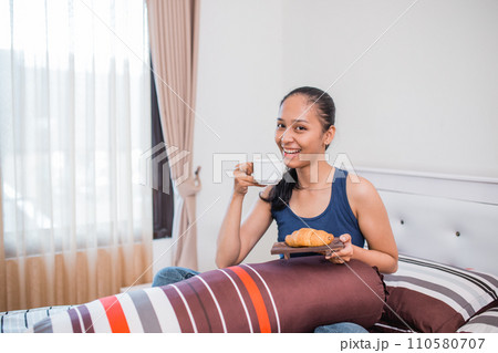 a smiling woman having breakfast sitting on a bed 110580707