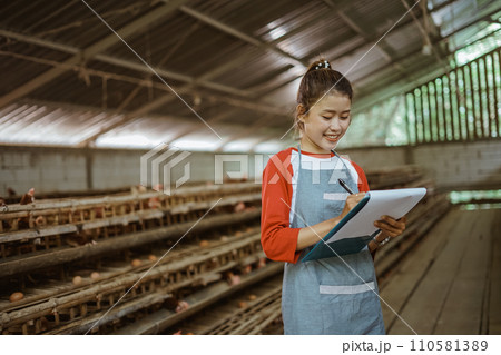 Asian female poultry farmer wearing apron writing something on clipboard Asian female poultry farmer wearing apron writing something on clipboard 110581389