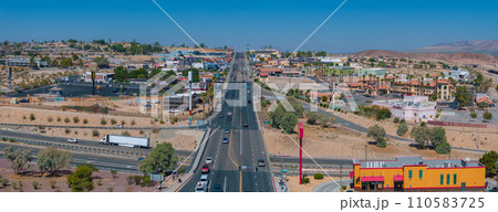 Aerial view of a bustling southwestern U.S. town, showcasing beige and brown buildings with terracotta roofs, amidst a clear, sunny desert landscape with a mountain backdrop. 110583725