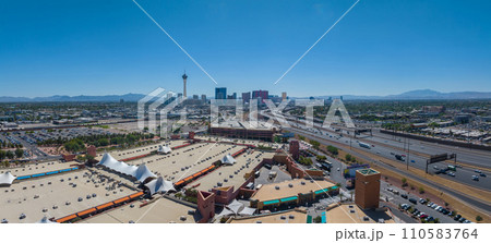 Aerial view of Las Vegas cityscape featuring the iconic Stratosphere Tower, diverse architecture, bustling roads, and green spaces against a mountainous backdrop in clear daylight. 110583764