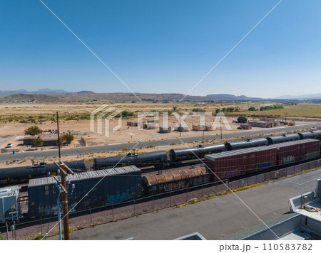 Captivating semi-arid landscape featuring a freight train with cargo containers and tankers, sparse desert vegetation, distant mountains, and clear blue skies, perfect for transportation themes. 110583782
