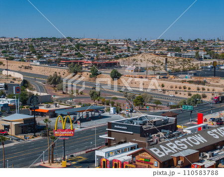 Elevated view of Barstow, California, capturing the bustling urban landscape, commercial brands, and traffic on Route 66, set against a backdrop of gentle hills and clear skies. 110583788