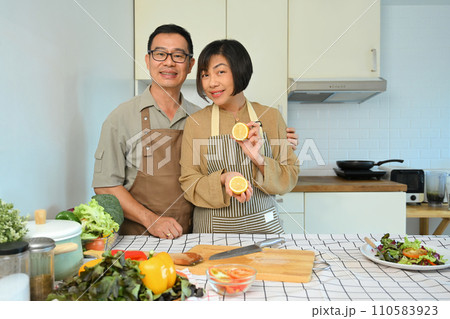 Happy retired couple in aprons cooking healthy food with organic ingredients in kitchen. Healthy lifestyle concept. 110583923