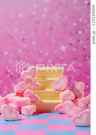 Heart-shaped marshmallows are displayed around a ladder-shaped platform. Sparkling pink background with pink and blue checkered surface. Front view, display. Heart-shaped marshmallows are displayed around a ladder-shaped platform. Sparkling pink background with pink and blue checkered surface. Front view, display. 110584006