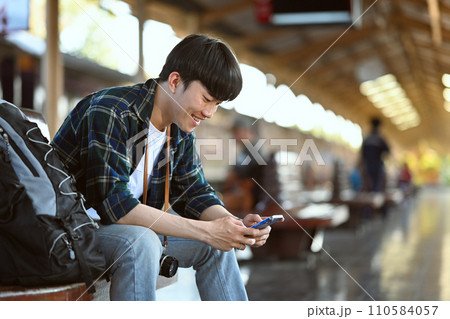 Handsome man backpacker using mobile phone at railway platform. Travel and vacations concept Handsome man backpacker using mobile phone at railway platform. Travel and vacations concept 110584057