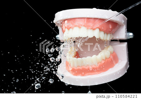 Artificial Tooth Plastic jaw clean with water spray jet. Teeth of dental jaw model spray with water to clean up before operation. Black background isolated. 110584221