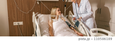 Doctor checking blood pressure of young woman patient in ward of modern clinic Doctor checking blood pressure of young woman patient in ward of modern clinic 110586189