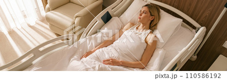 Woman patient lying on bed at modern hospital ward after surgery. Health care and medicine concept Woman patient lying on bed at modern hospital ward after surgery. Health care and medicine concept 110586192