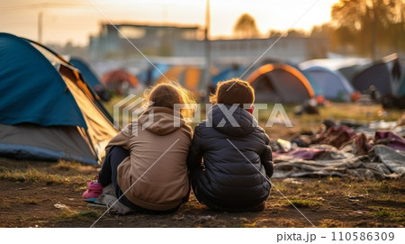Group of refugee kids waiting in a refugee camp. Portrait of poor caucasian refugees at the borderline. Impoverished refugees escaping war. Young kids playing outside a refuge camp. Group of refugee kids waiting in a refugee camp. Portrait of poor caucasian refugees at the borderline. Impoverished refugees escaping war. Young kids playing outside a refuge camp. 110586309