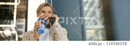 Female entrepreneur talking phone while drinking coffee standing on office building background Female entrepreneur talking phone while drinking coffee standing on office building background 110586338
