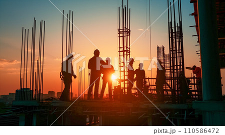 日の出時、建設現場で設計図を議論する建設チーム、夜明けの空に映えるシルエット。 日の出時、建設現場で設計図を議論する建設チーム、夜明けの空に映えるシルエット。 110586472
