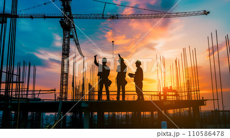 日の出時、建設現場で設計図を議論する建設チーム、夜明けの空に映えるシルエット。 110586478