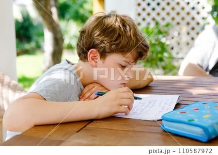 Hard-working sad school kid boy making homework during quarantine time from corona pandemic disease. Upset tired child on home schooling in coronavirus covid time, schools closed. Dad on background Hard-working sad school kid boy making homework during quarantine time from corona pandemic disease. Upset tired child on home schooling in coronavirus covid time, schools closed. Dad on background 110587972