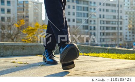 Legs of a businessman in fashionable shoes walking outdoors. Business concept. Close-up view to the businessman in a black new shoes walks on the street. Stylish men wears. Low angle 110588428