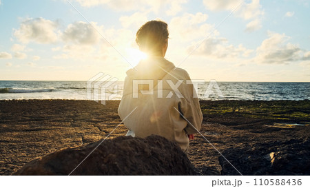 Man on a beach is looking distance during beautiful summer sunset. Human looks to the sun over horizon in the morning while sunrise. Happy person contemplates the beauty of nature. Freedom concept. 110588436