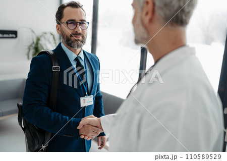 Pharmaceutical sales representative shaking hands with doctor in medical building. Doctor greeting hospital director, manager in private clinic. Pharmaceutical sales representative shaking hands with doctor in medical building. Doctor greeting hospital director, manager in private clinic. 110589529