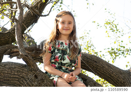 Cute five-year-old girl sitting on a tree in the summer in nature 110589590