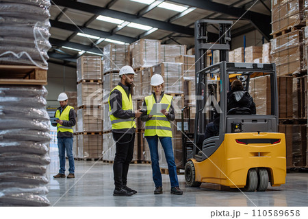 Warehouse workers reading product order, order picking. Warehouse manager checking delivery, stock in warehouse, inspecting products for shipment. 110589658