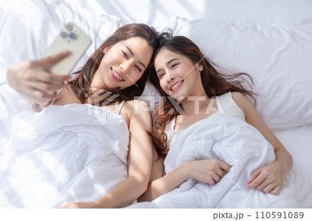 Affectionate and filled with happiness, the couple takes selfie on cozy bed, showcasing the genuine connection and love they share heartwarming beautiful moment between an LGBTQ couple Affectionate and filled with happiness, the couple takes selfie on cozy bed, showcasing the genuine connection and love they share heartwarming beautiful moment between an LGBTQ couple 110591089