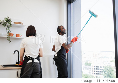African washing windows with mop, listening to music in headphones and dancing. 110591360