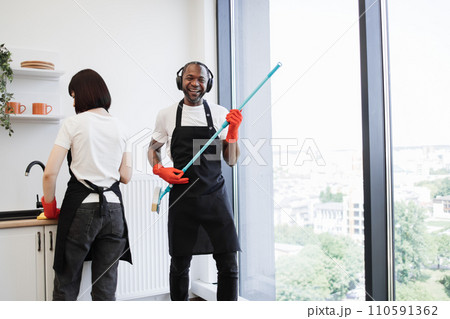 African male worker washes windows, having fun while holding mop like guitar. African male worker washes windows, having fun while holding mop like guitar. 110591362