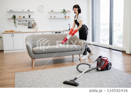 Full length of young cleaner vacuuming sofa with portable vacuum cleaner. Full length of young cleaner vacuuming sofa with portable vacuum cleaner. 110592416