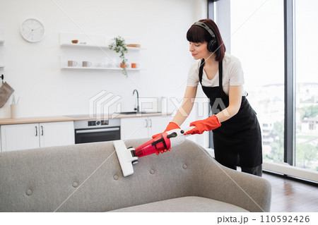 Professional young cleaner vacuuming sofa with portable cordless vacuum cleaner. Professional young cleaner vacuuming sofa with portable cordless vacuum cleaner. 110592426