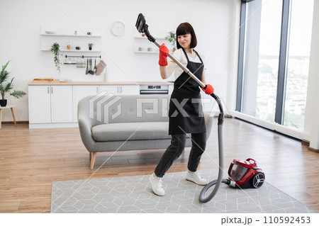 Happy female cleaning service worker cleaning home while listening to music. Happy female cleaning service worker cleaning home while listening to music. 110592453