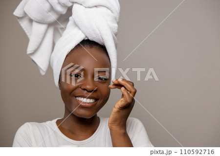 Cheerful attractive woman with towel on head doing daily skincare routine with cream moisturizing 110592716